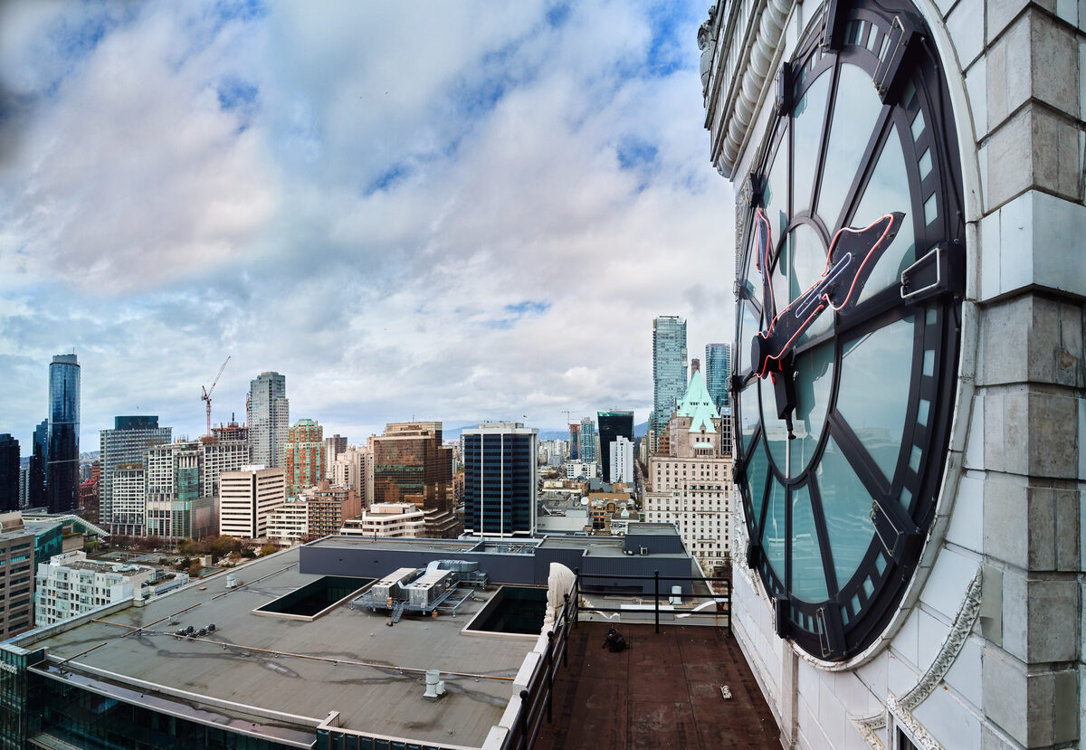 The Vancouver Block clock face framing the downtown skyline at golden hour